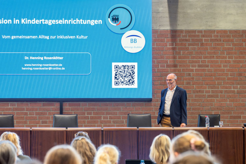 Dr. Henning Rosenkötter steht vor am Pult hinter ihm ist die Präsentation zu Inklusion an Kindertageseinrichtungen zu sehen